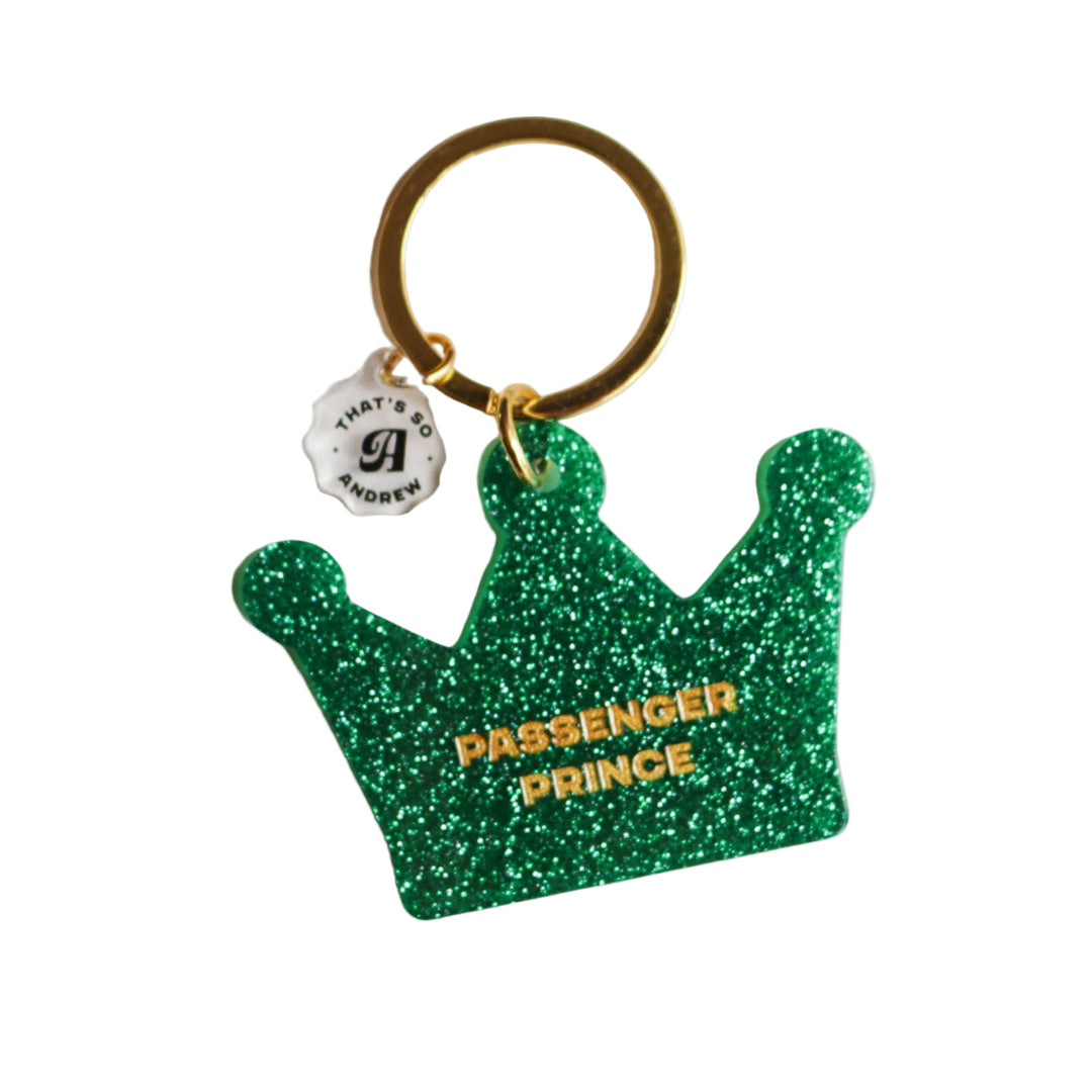 A green, glittery acrylic keychain in the shape of a crown with the text 'PASSENGER PRINCE' on it, attached to a metal keyring. 