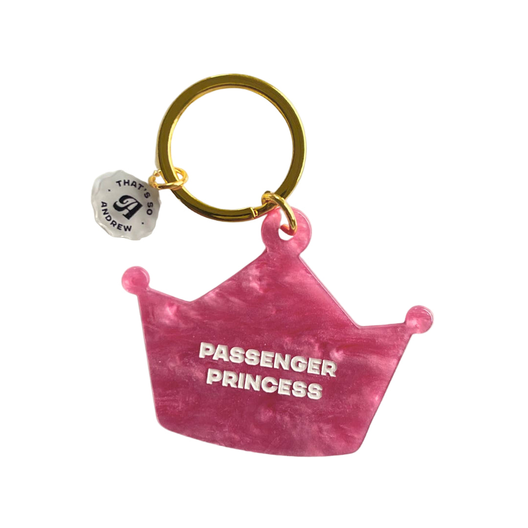 A pink acrylic keychain in the shape of a crown with the text 'PASSENGER PRINCESS' engraved on it. It has a gold-colored keyring.