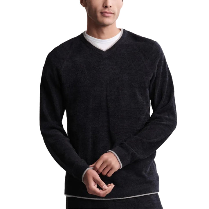 Man wearing a dark gray sweater over a white shirt on a plain background