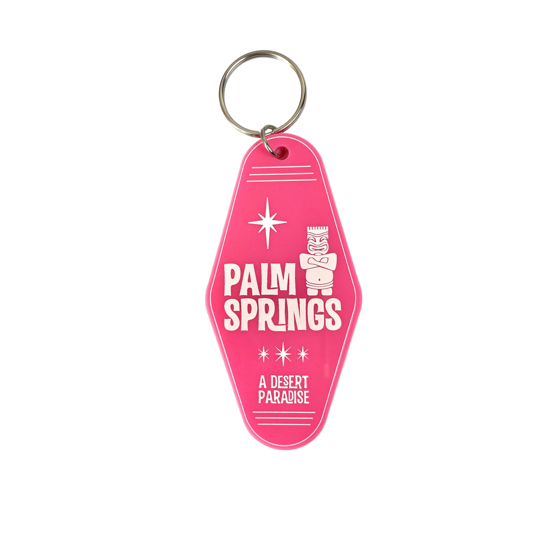 A hot pink keychain with 'Palm Springs A Desert Paradise' embossed on it, featuring a white tiki head and star motifs.