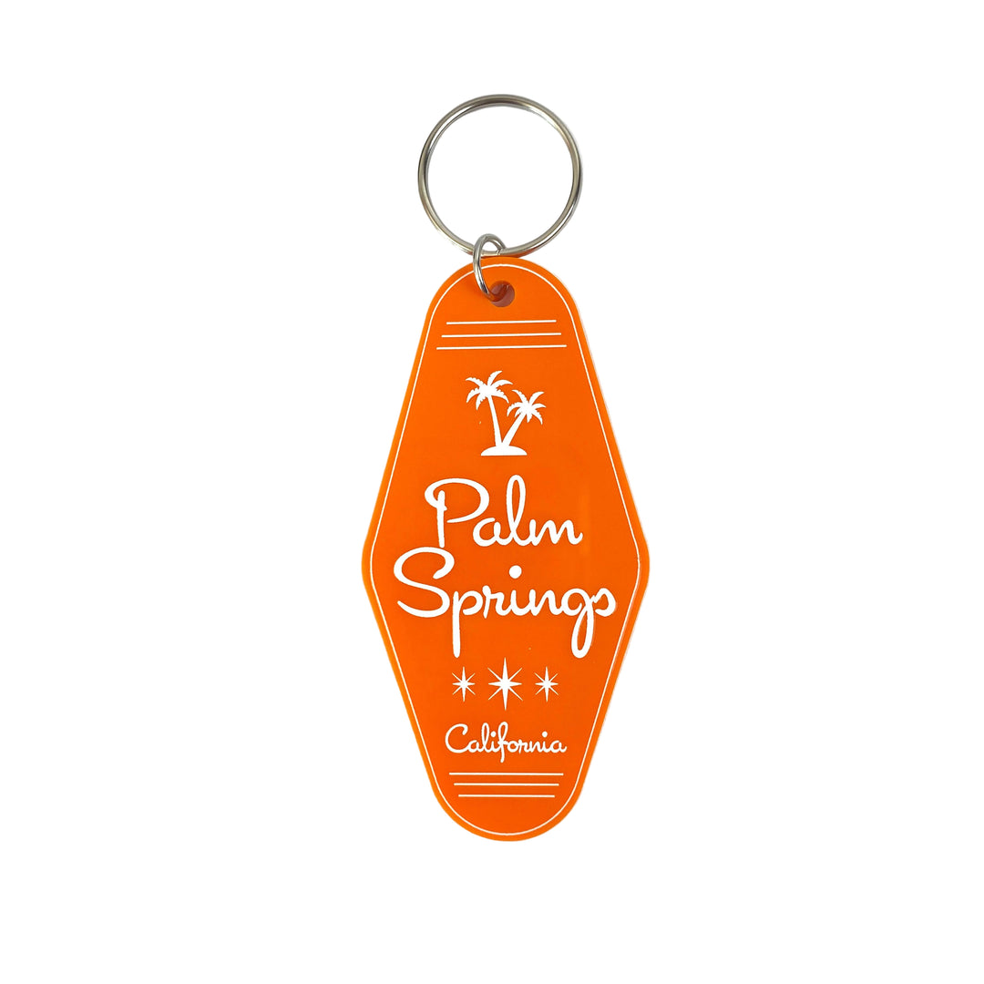 An orange keychain with 'Palm Springs California' embossed on it, shaped like a vintage motel key tag.