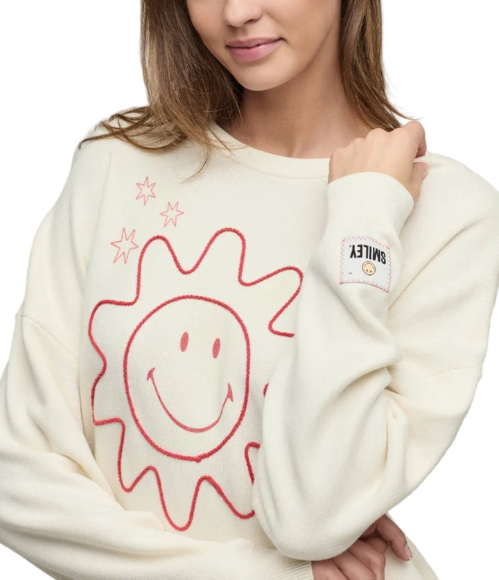 Woman wearing a cream-colored sweater with a red sun design on a plain background